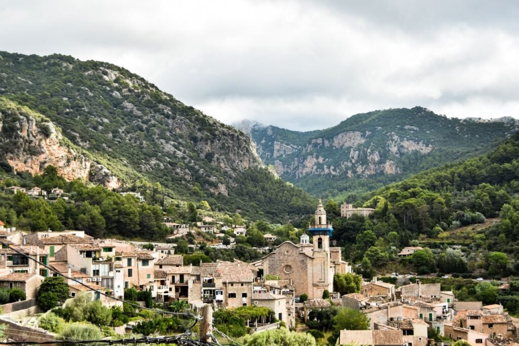 Scenic view of a quaint village nestled in lush green mountains under a cloudy sky.