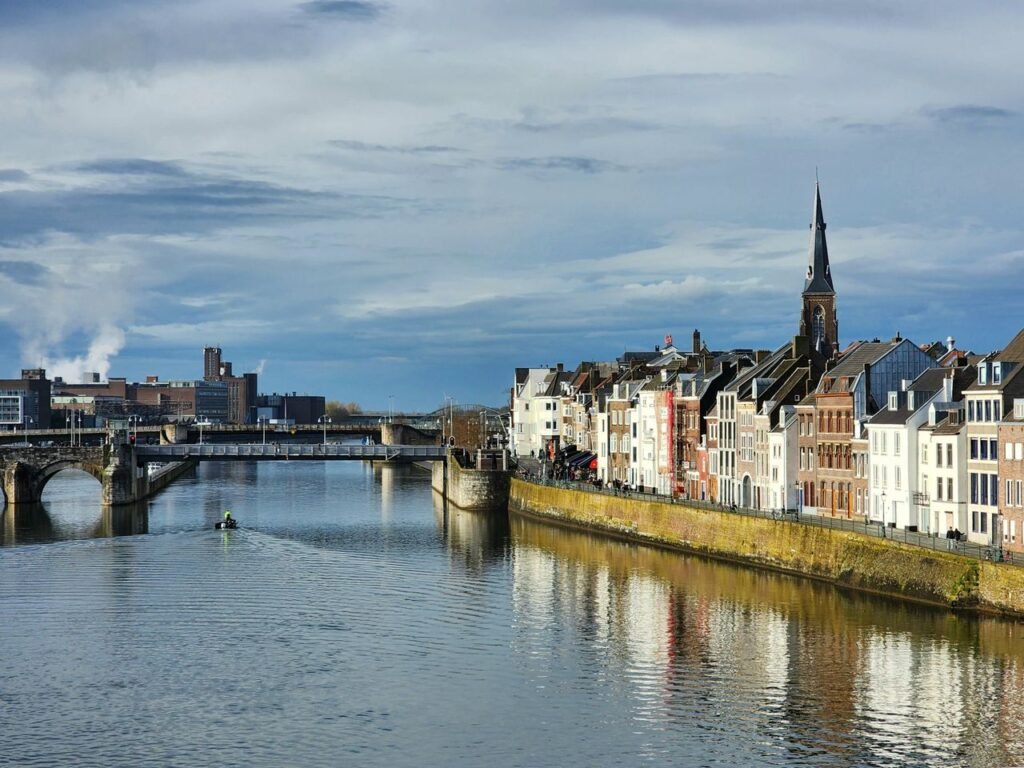 إطلالة خلابة على البيوت التاريخية وجسر سينت سيرفاسبروك (Sint Servaasbrug) على نهر الموز (Meuse) تحت سماء غائمة في مدينة ماستريخت بهولندا